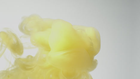 Yellow-Paint-Or-Dye-Dropped-Into-Water-Against-White-Background-To-Create-Swirling-Colourful-Smoke-Background